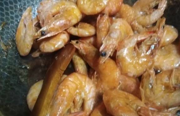 Замороженные неочищенные креветки с чесноком и соевым соусом на сковороде